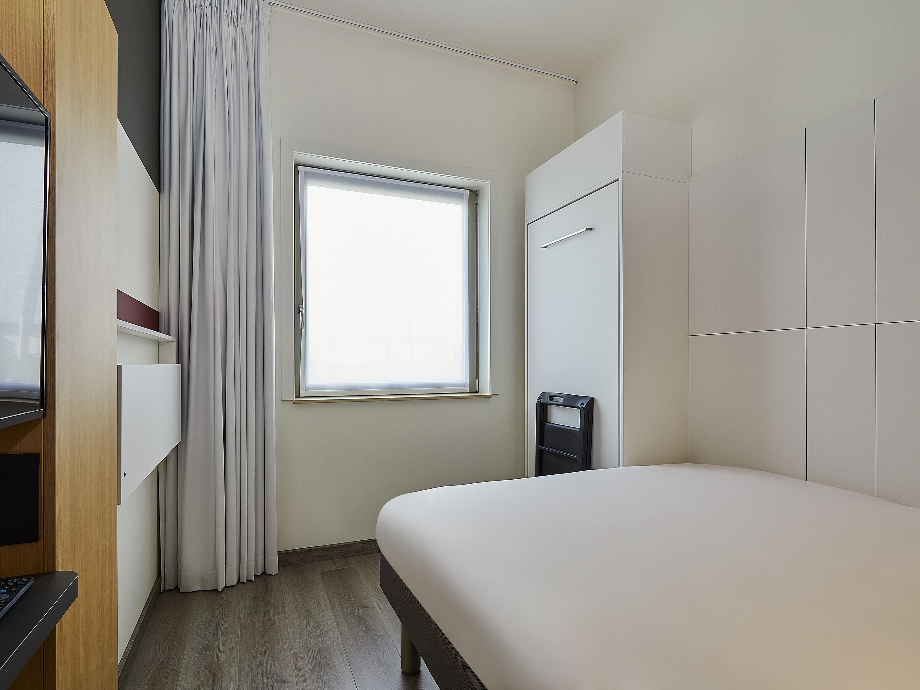 Une chambre d’hôtel avec un lit, une télévision, une fenêtre avec des rideaux et une armoire.