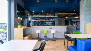 Un espace bar moderne comprenant un comptoir, des tabourets et un coin salon avec des tables et des chaises.