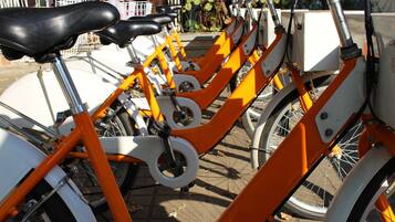 Une rangée de vélos d’appartement, avec des cadres orange et des selles blanches, est stationnée dans un espace extérieur.
