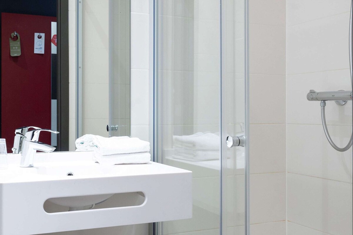 Une salle de bain moderne avec une douche à l’italienne en verre, un lavabo blanc doté d’un robinet chromé et un mur d’accent rouge.