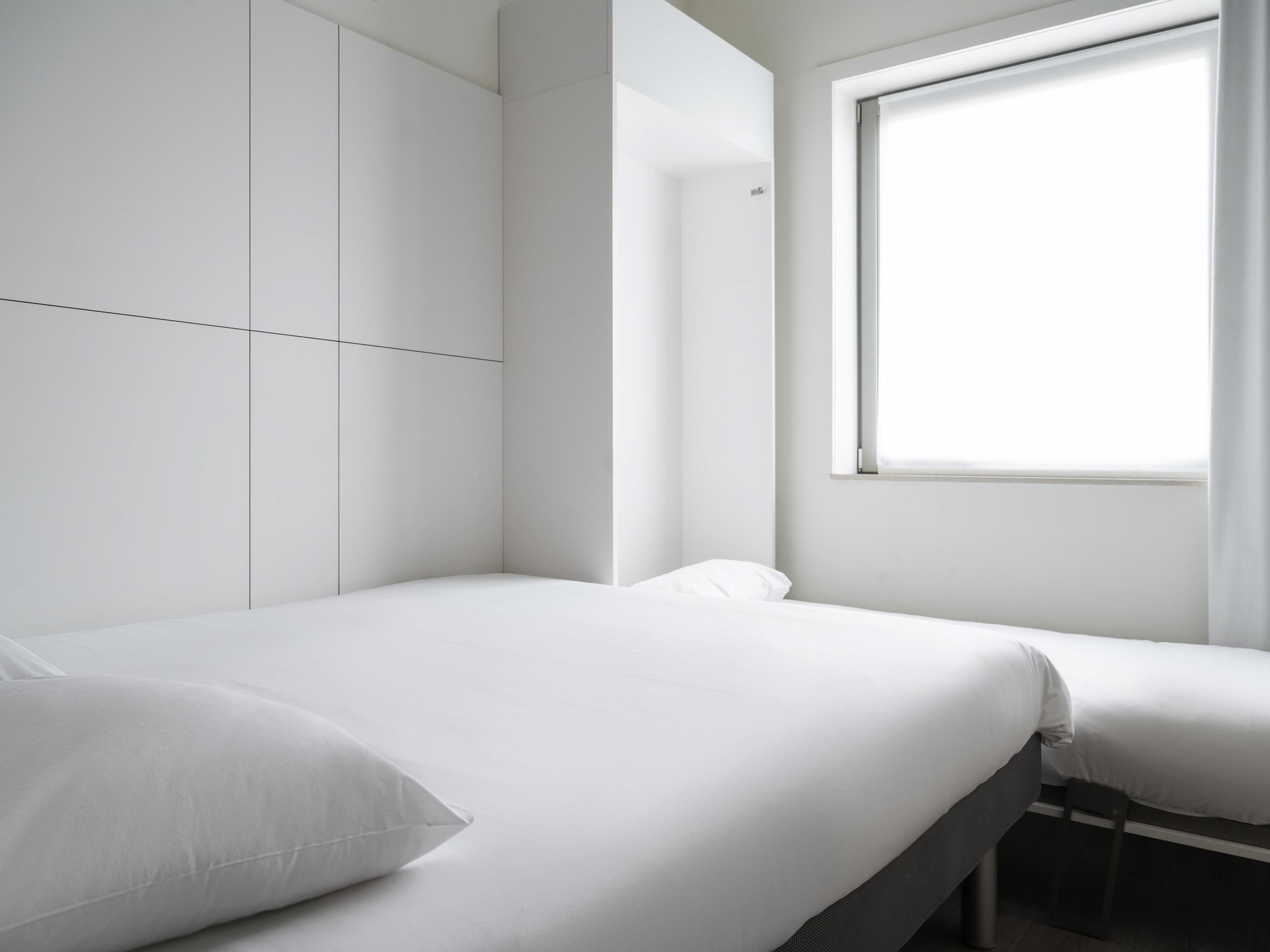 Une pièce minimaliste comprenant un lit, une fenêtre et une armoire.