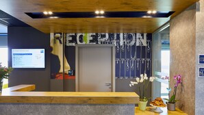 Un espace d’accueil avec un comptoir en bois, un écran d’ordinateur affichant un site web et deux orchidées en pot.