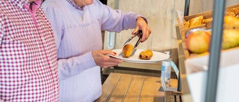A person serving food from a tray to another person at a wooden table.