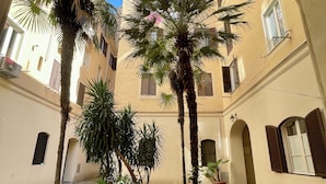 Un patio con palmeras y muros cubiertos de hiedra, rodeado de edificios con balcones y ventanas.