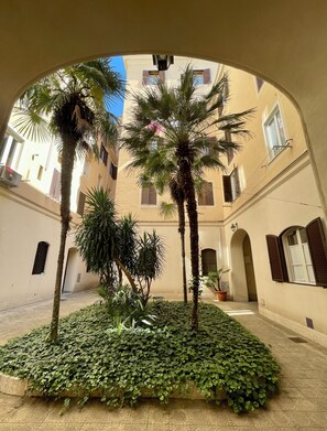 Stroll through a serene courtyard surrounded by lush greenery and classical architecture with arched doorways.