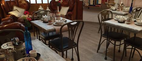 A cozy dining area with wooden tables and chairs, a leather sofa, and a bookshelf filled with books.