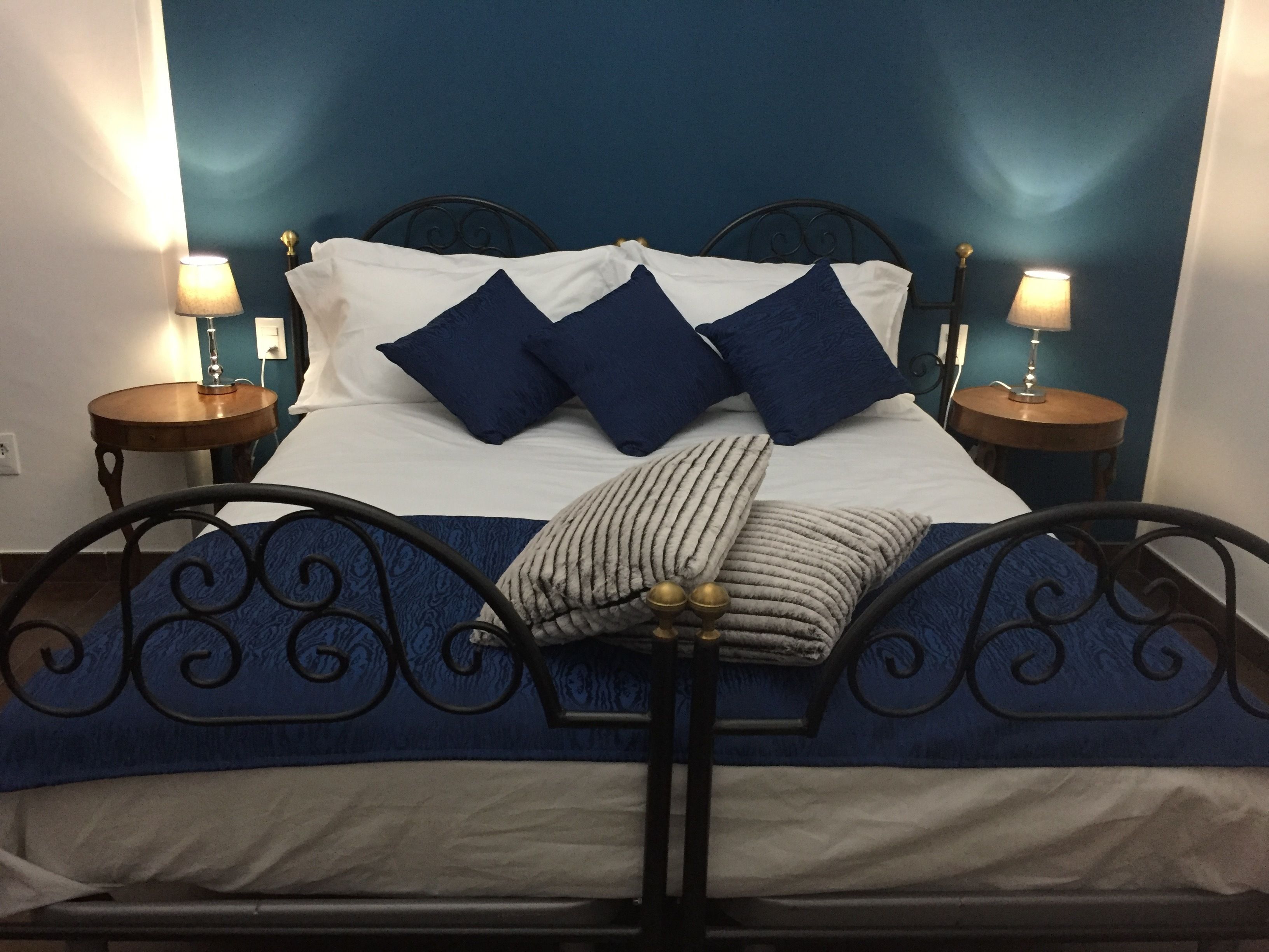 Un lit avec un cadre en métal, une literie blanche et des oreillers bleus. Il y a deux tables de chevet avec des lampes.