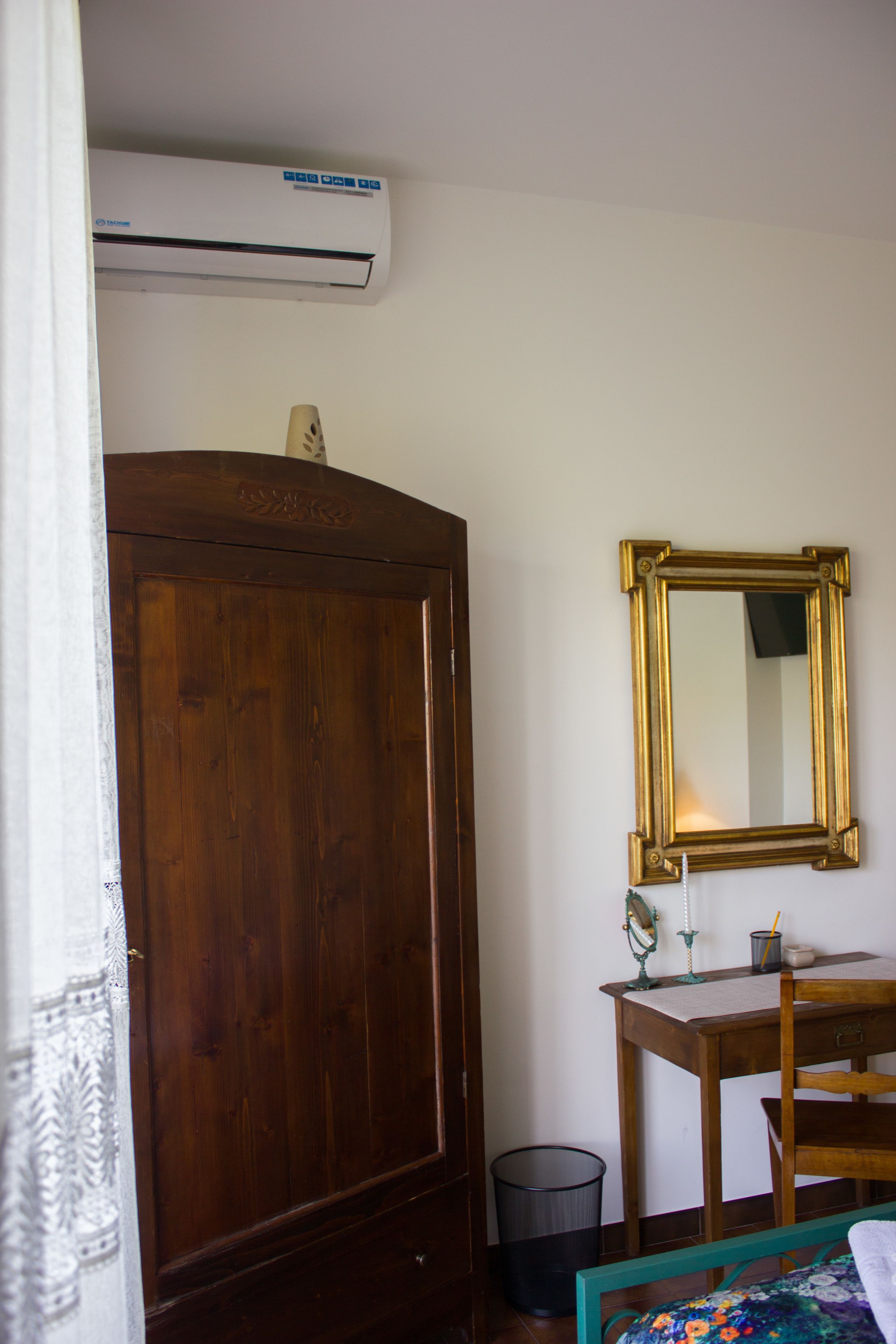 A bedroom with a wooden wardrobe, a small table with a mirror, and a bed with a floral bedspread.