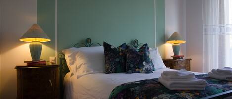 A neatly made bed with a floral bedspread, two bedside lamps, and a small wooden nightstand with books.
