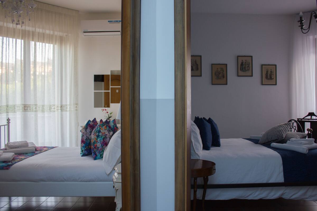 A hotel room with two beds, a mirror, a chandelier, and artwork on the wall.