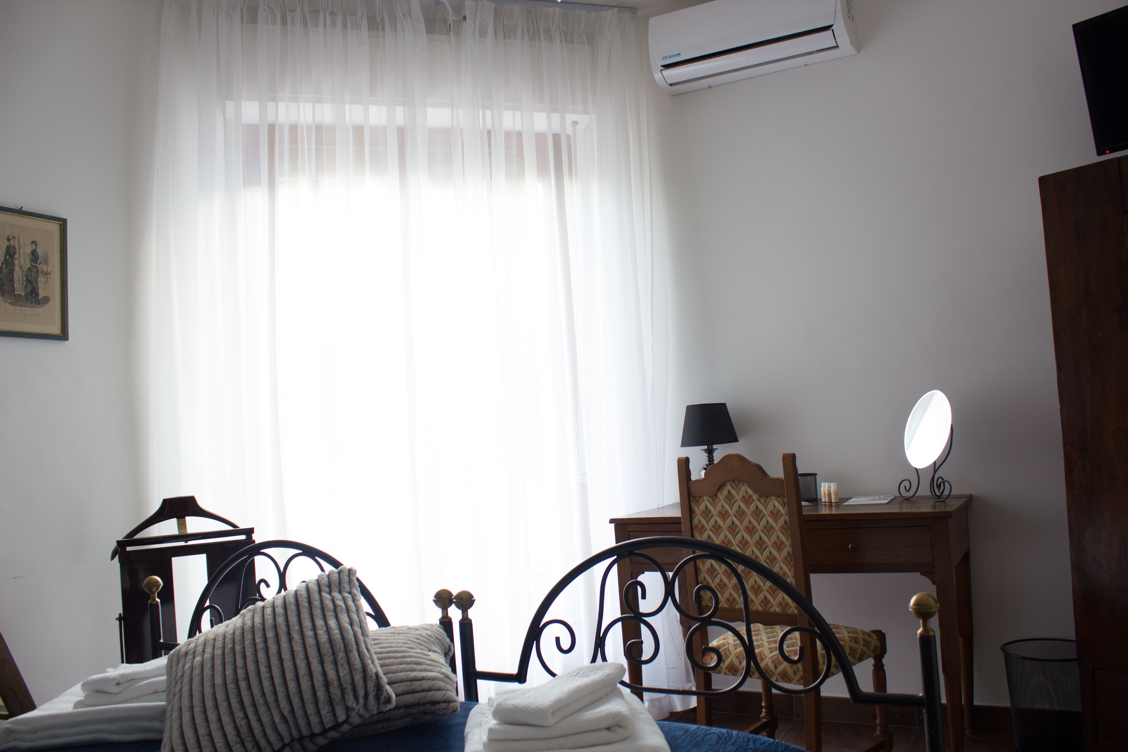 A bedroom with a bed, a chair, a desk with a mirror, and an air conditioner.