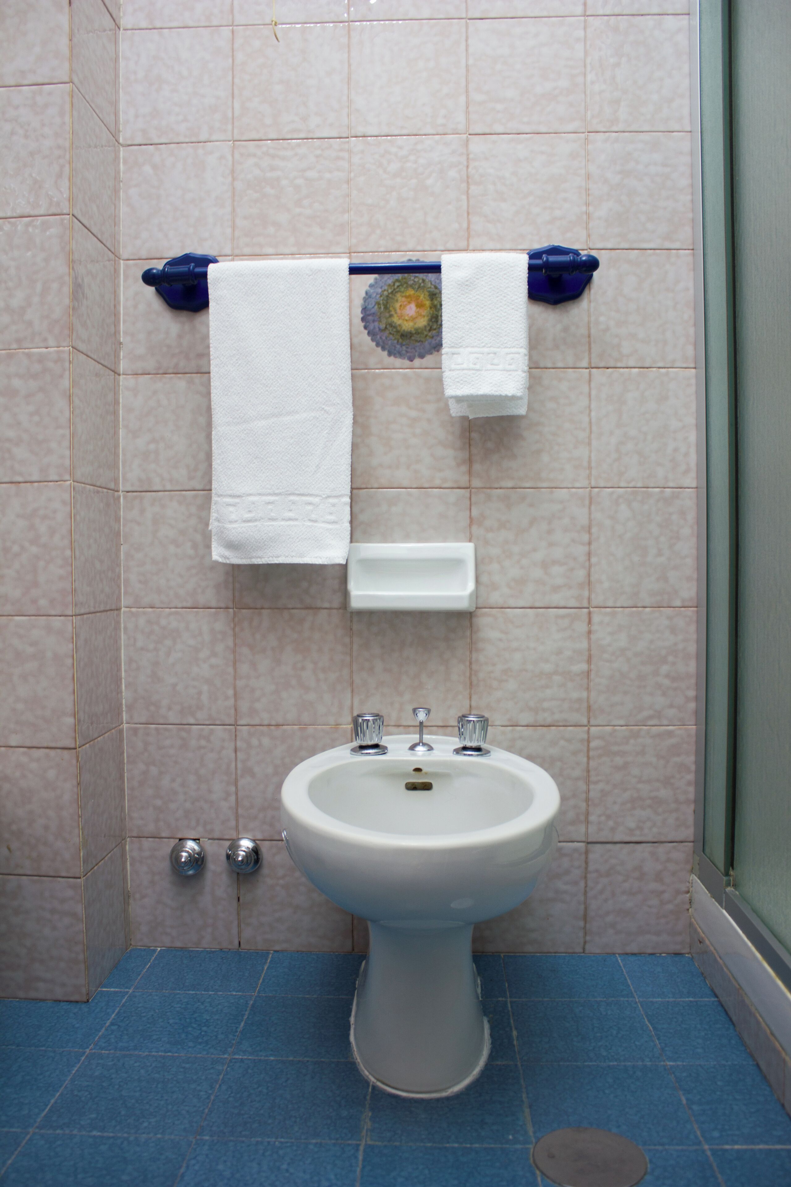 A bathroom with a white pedestal sink, two faucets, and a blue floor.