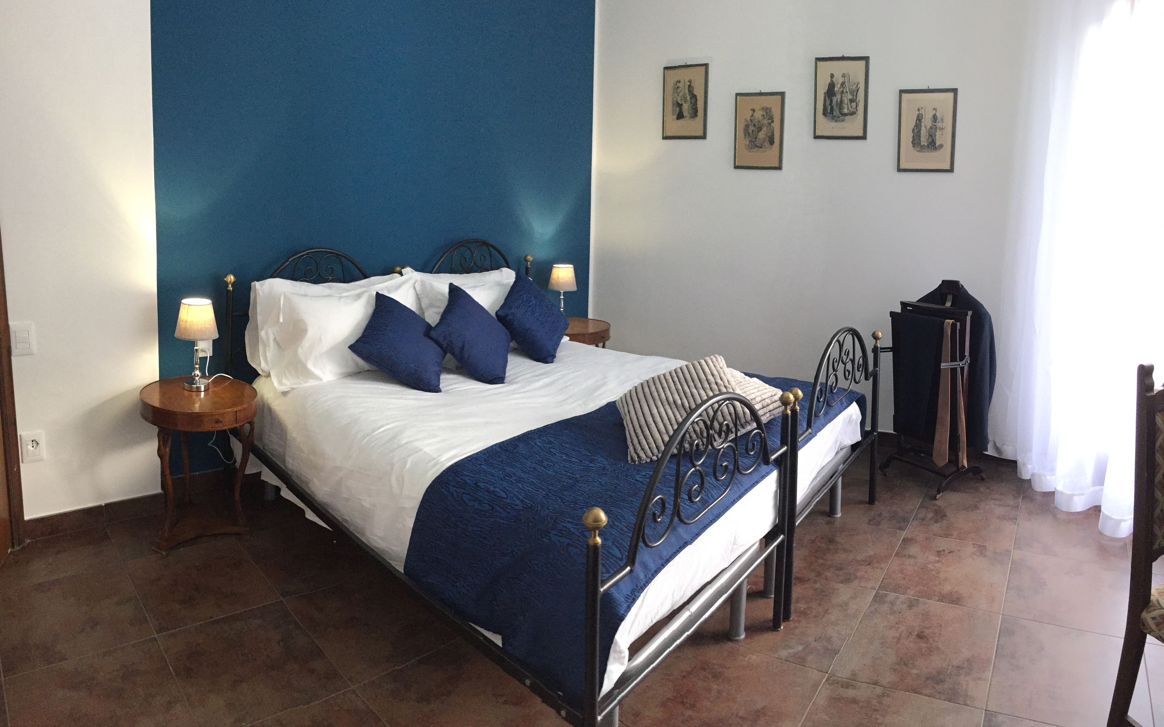 Ein Schlafzimmer mit einem Bett, zwei Nachttischen mit Lampen, einem blauen Kopfteil und drei gerahmten Bildern an der Wand.