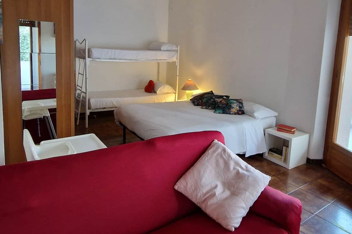 A room with a red sofa, a bunk bed, a desk with a lamp, and a small white table with a book.