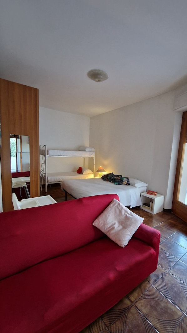 A room with a red sofa, a bunk bed, a desk with a lamp, and a small white table with a book. - City View Pescara (Pescara)