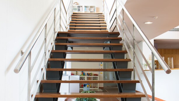 A modern staircase with wooden steps and metal railings, leading to a landing area with a white wall and a blue sign. - Hotel Rural Santo António (Arronches)