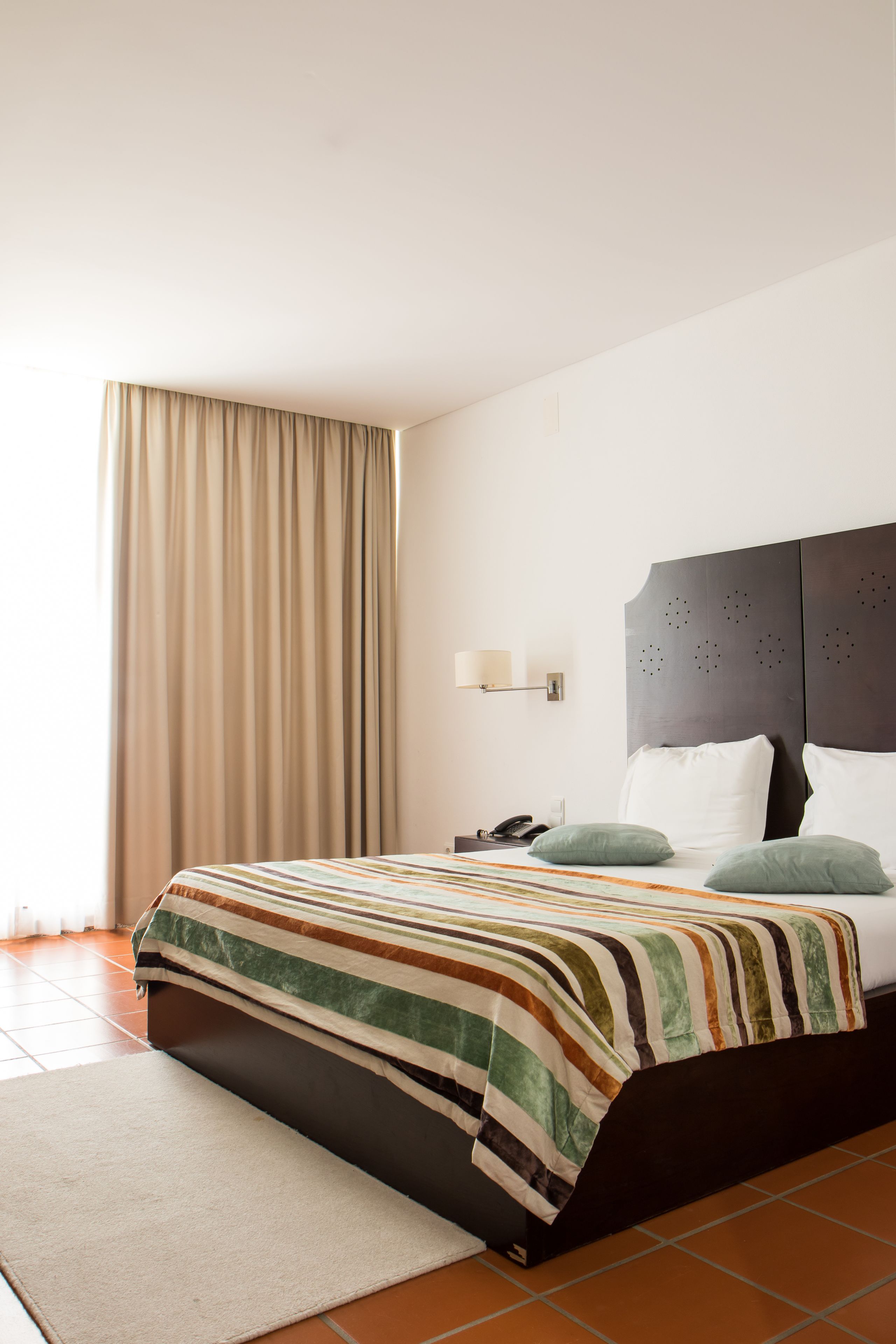 A hotel room with a bed, a nightstand, a telephone, and a window with curtains.