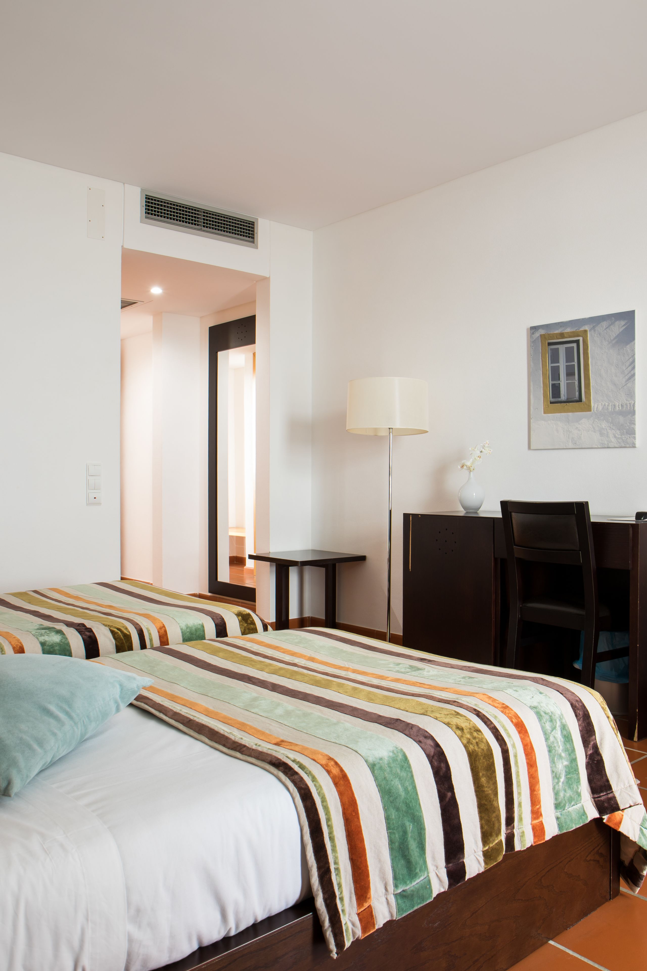 Habitació d'hotel amb dos llits, escriptori, cadira, làmpada i un quadre a la paret.