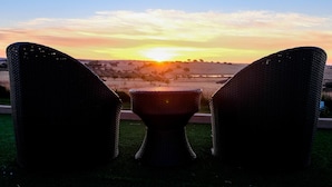 Two wicker chairs facing a sunset over a grassy field. - Hotel Rural Santo António (Arronches)