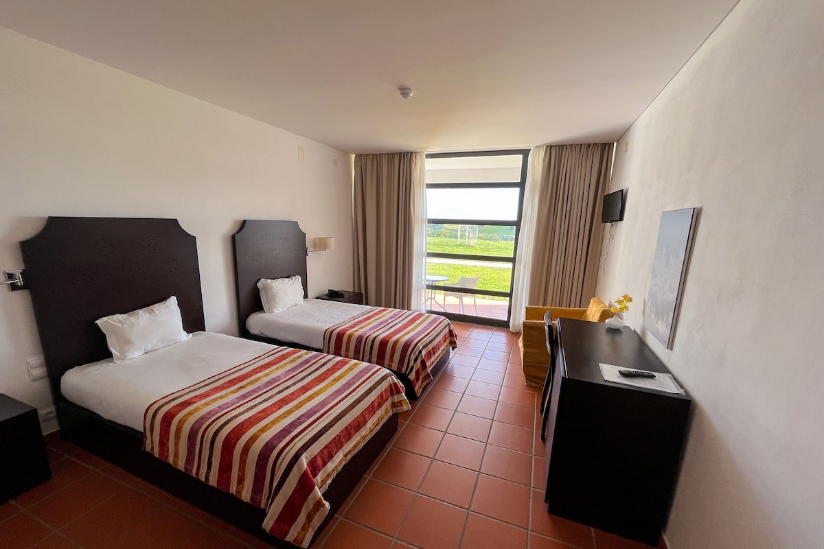 Ein Hotelzimmer mit zwei Betten, einem Schreibtisch, einem Stuhl und Blick ins Freie.