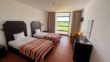 Ein Hotelzimmer mit zwei Betten, einem Schreibtisch, einem Stuhl und Blick ins Freie.