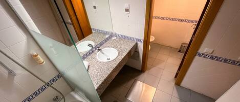 A bathroom with two sinks, a mirror, a shower, and a toilet.