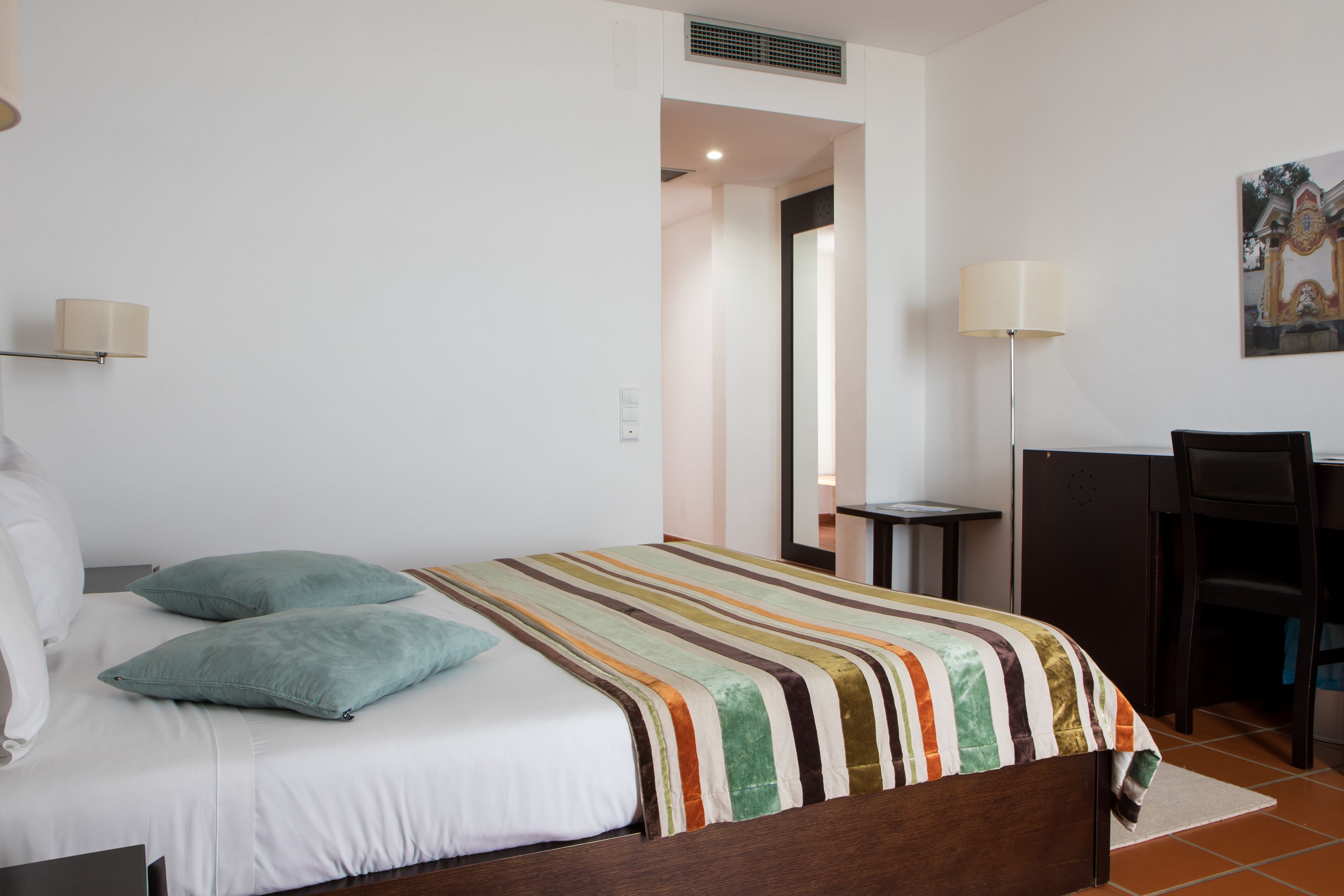 Habitación de hotel con cama, escritorio y silla. Hay una ventana y una puerta.