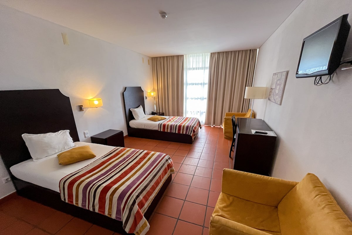Ein Hotelzimmer mit zwei Betten, einem Schreibtisch, einem Stuhl und einem Fernseher.