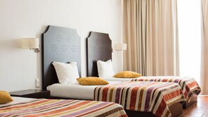 A hotel room with two beds, a nightstand, and a window with curtains. - Hotel Rural Santo António (Arronches)