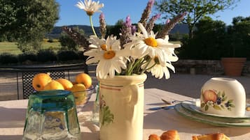 Uma mesa com um vaso de margaridas brancas, um pote de vidro e um prato com pão.