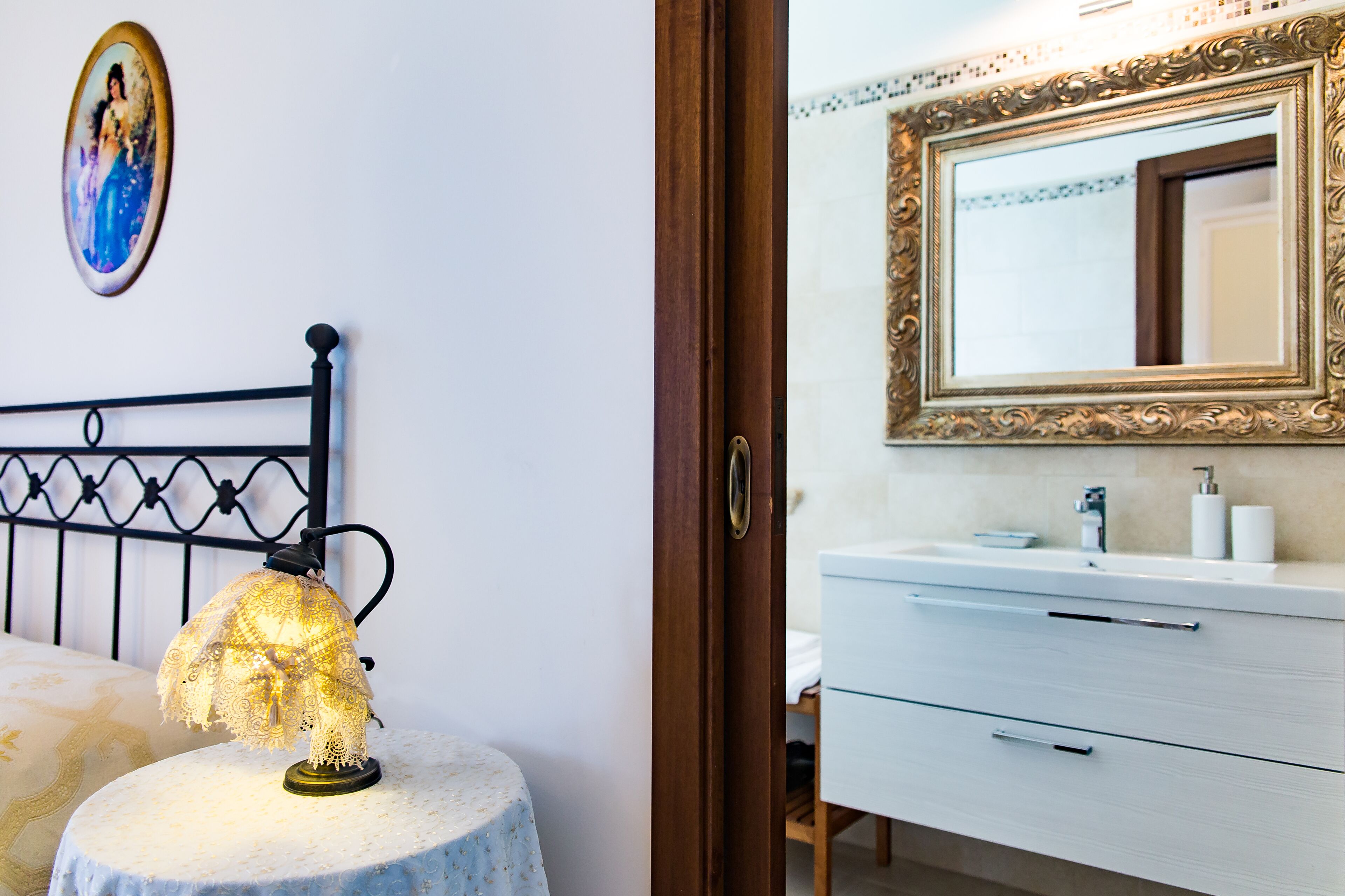 Un dormitorio con cama, lámpara de noche, una mesita redonda, cómoda y espejo.