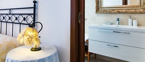 Un dormitorio con cama, lámpara de noche, una mesita redonda, cómoda y espejo.