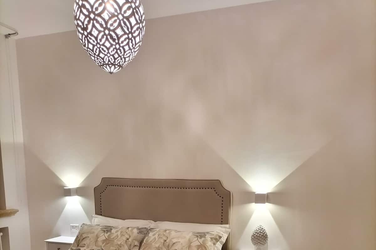 A bedroom with a large bed, two bedside tables, a nightstand, a decorative hanging light, and a sofa.