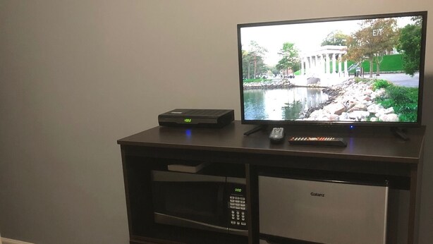 A dark wooden entertainment center with a flat-screen TV, a DVD player, and a microwave. - The Guest House (Circleville)