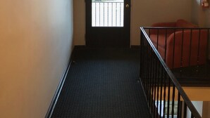 A hallway with a door leading to an outdoor area, a window with a stone facade, and a red chair. - The Guest House (Circleville)