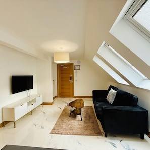 Un salon moderne avec un téléviseur à écran plat, un canapé noir, une porte en bois et une lucarne.