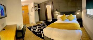A hotel room with a bed, a desk, and a chair. There is a door leading to another room.