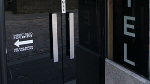 En hotelindgang med en glasdør, et træk håndtag og instruktioner til kortindføring og brug af knap til at tilkalde personale.