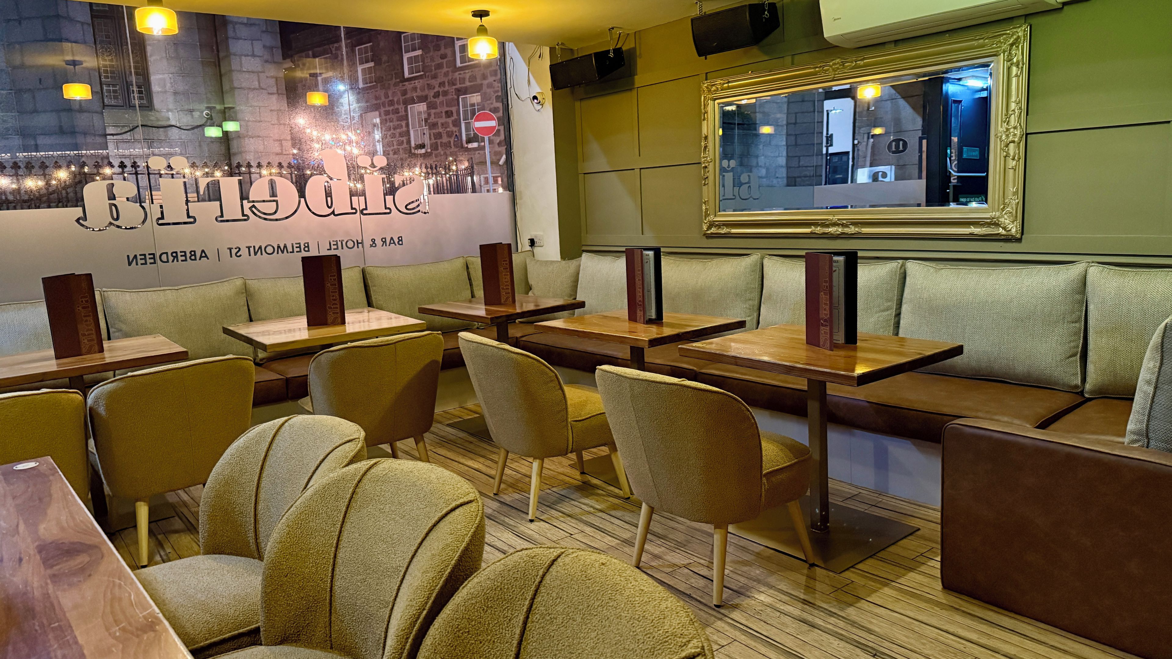 A restaurant interior with booths and tables, a cityscape mural, and a framed mirror on the wall.