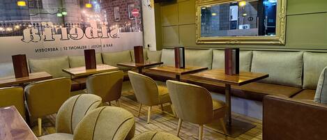 A restaurant interior with booths and tables, a cityscape mural, and a framed mirror on the wall.