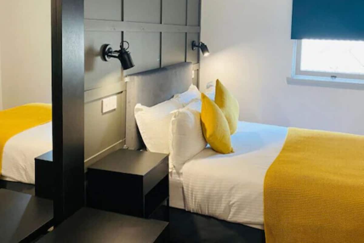 A hotel room with two beds, a headboard, bedside tables, and a window with blinds.