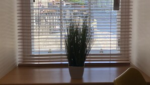 Et vindue med vandrette persienner, en potteplante og en radiator nedenunder.