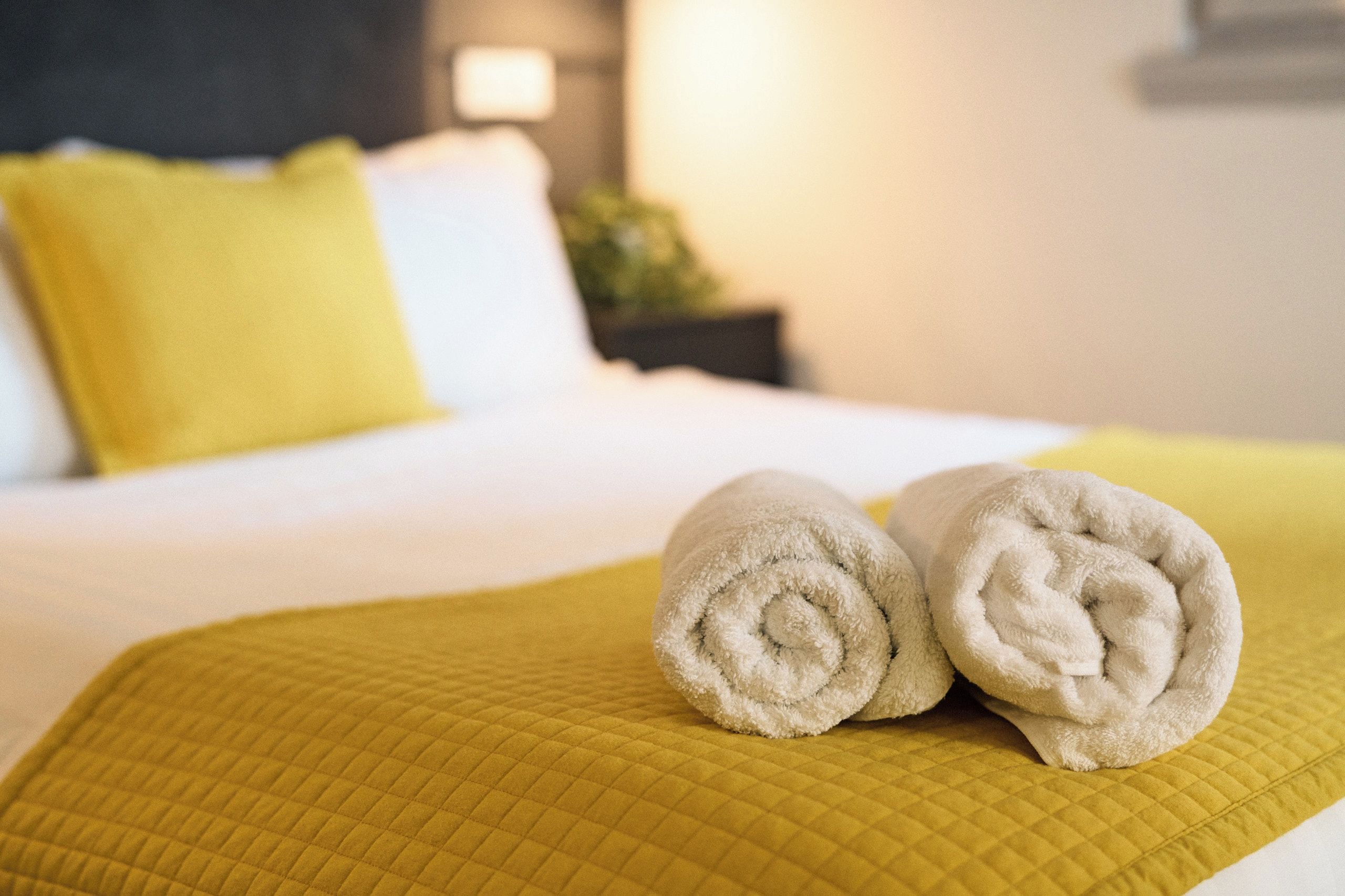 A bed with a quilted yellow bedspread and two rolled towels on it.