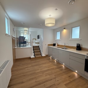 Eine moderne Küche mit Holzboden, einer Treppe und einem Essbereich, der durch eine offene Tür sichtbar ist.