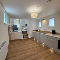 Moderni keittiö, jossa on puulattia, portaikko ja ruokailutila, joka näkyy avoimen oven läpi.