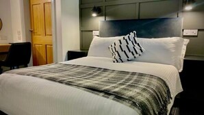 Et hotelværelse med en stor seng, en sengegavl, et skrivebord og en stol.