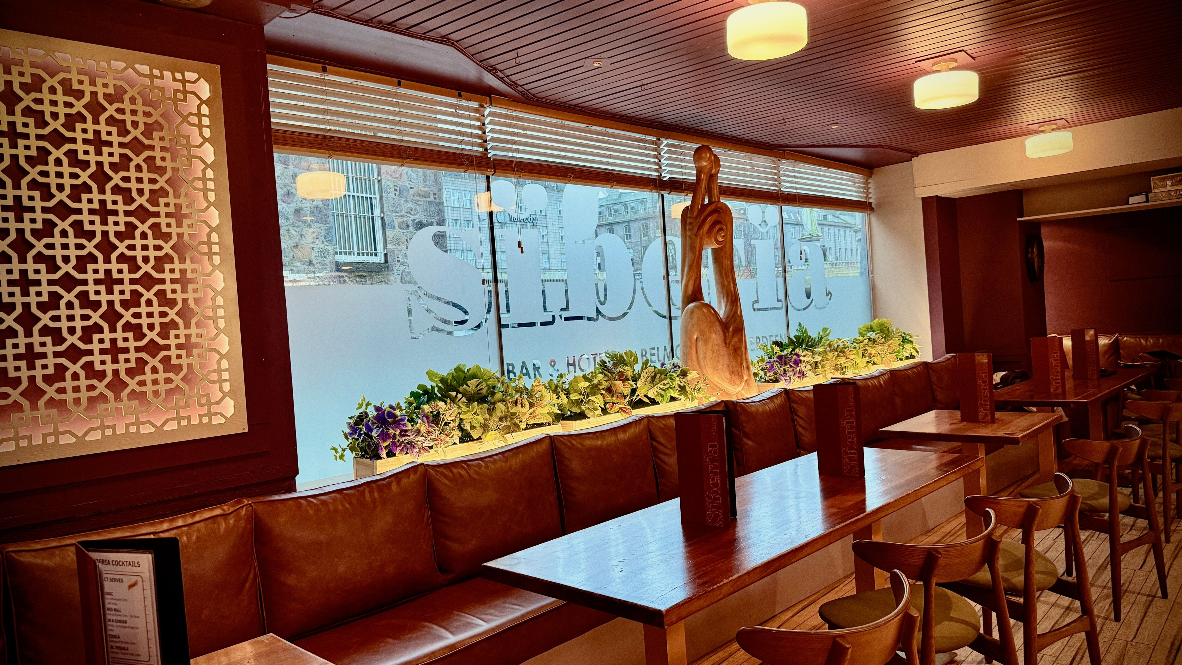 A restaurant interior with wooden benches, a decorative wall, and a view through the window.