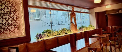 A restaurant interior with wooden benches, a decorative wall, and a view through the window.