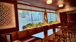 L’intérieur d’un restaurant avec des bancs en bois, un mur décoratif et une vue par la fenêtre.