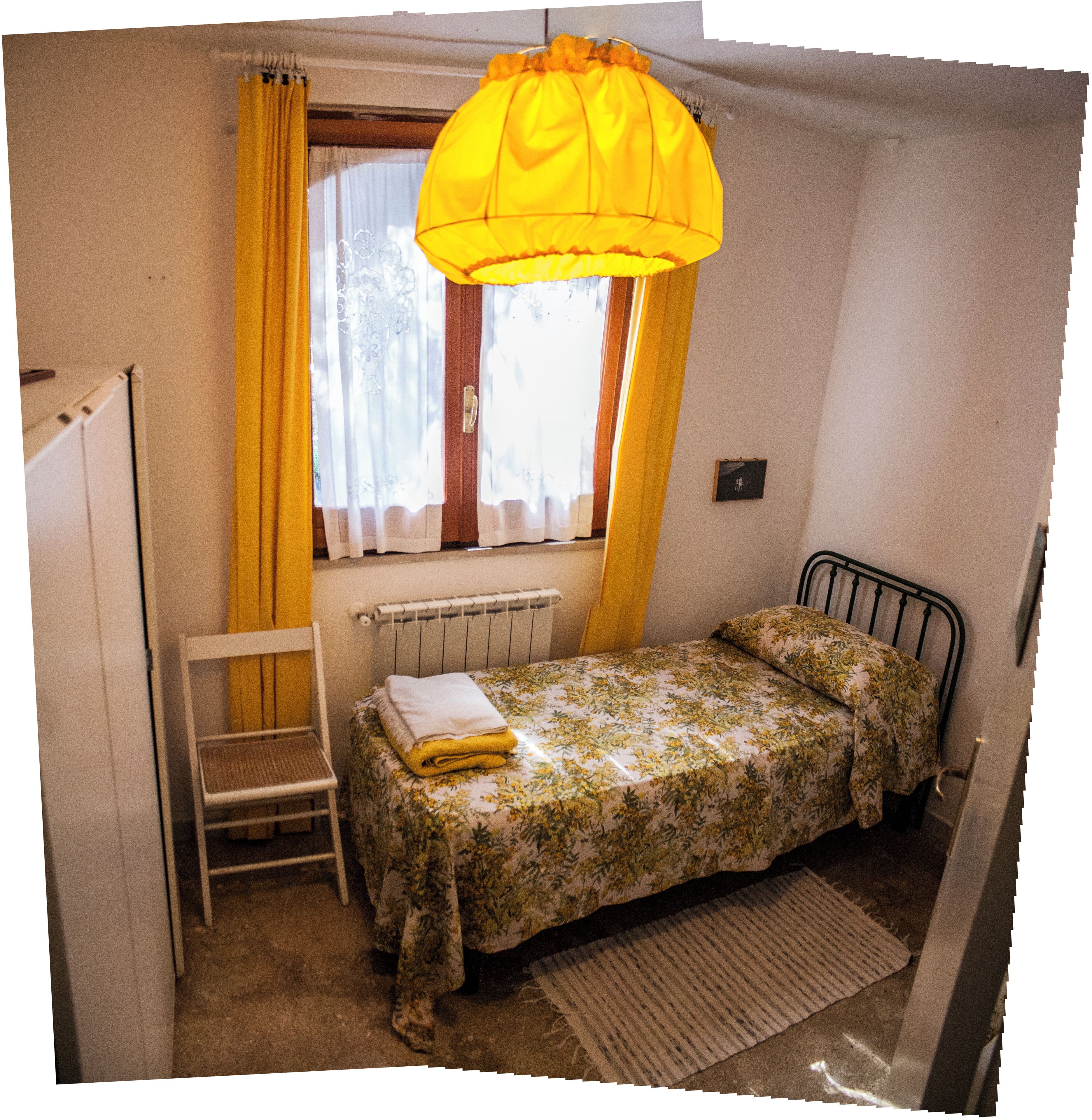 A small bedroom with a single bed, a radiator, a chair, and a window with curtains.